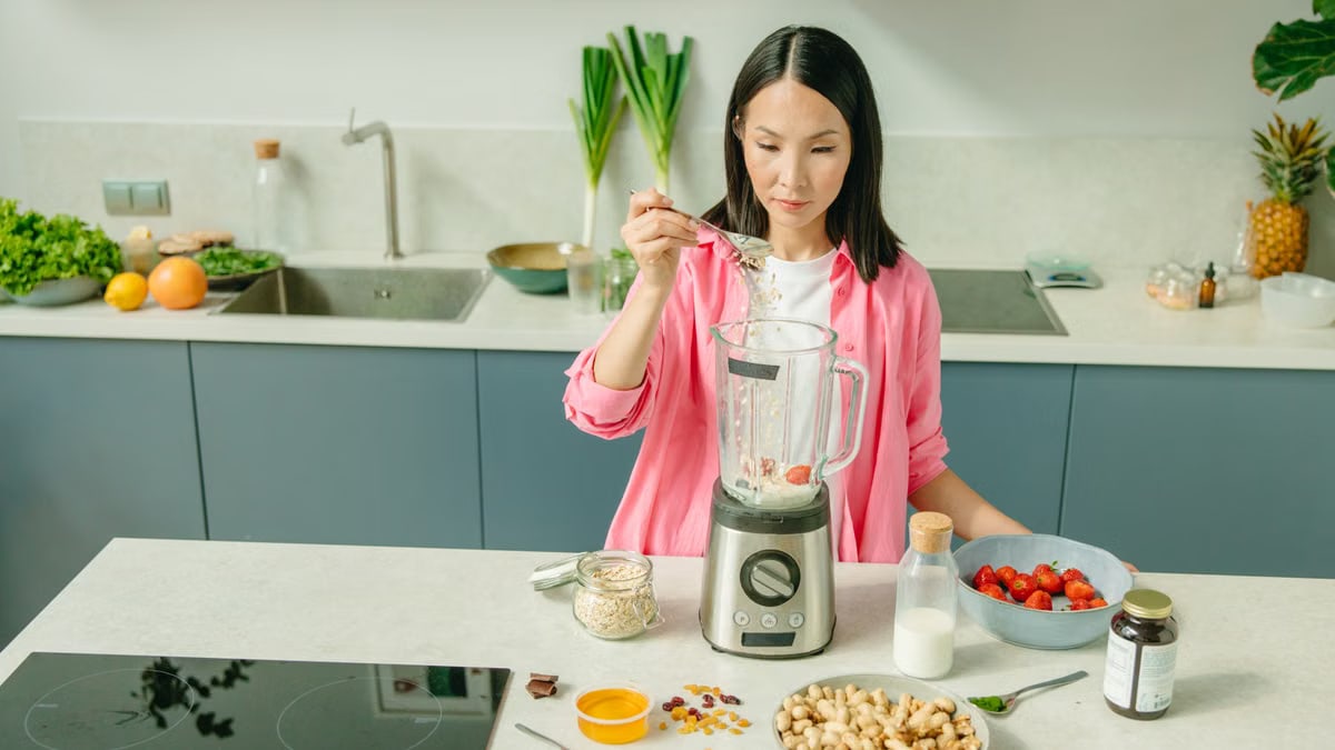 A woman in a kitchen preparing a nutritious smoothie with fresh ingredients.